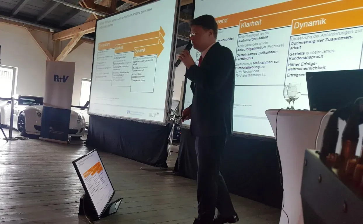 Firmenpräsentation in einer großen Halle mit Bühne, Mikrofon und großen Bildschirmen