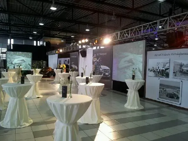 Ein großer Saal mit vielen bezogenen Stehtischen und einem großen Bildschirm zur Liveübertragung