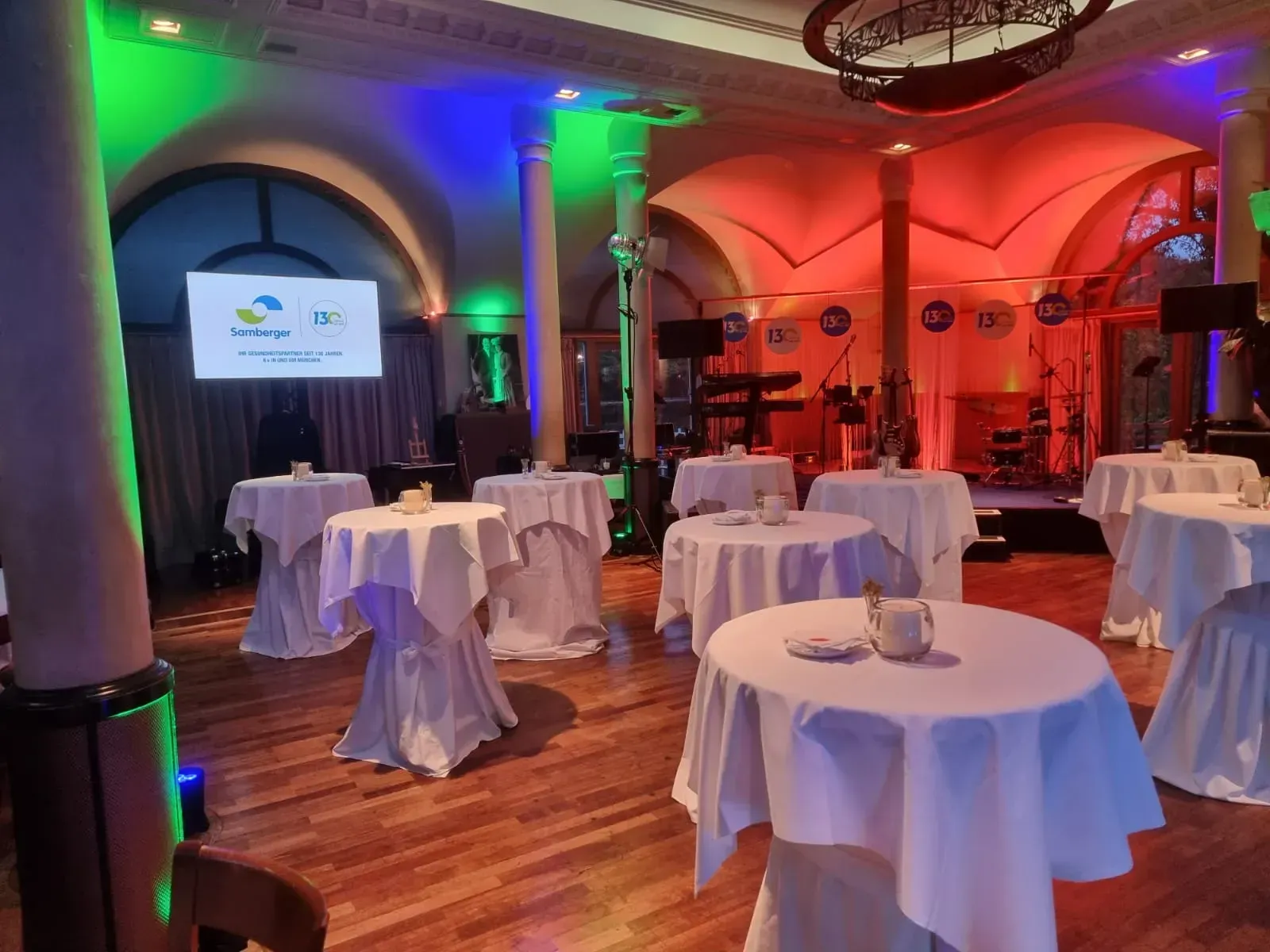 Großer Saal mit eingedeckten Tischen und einer kleinen Bühne im Hintergrund