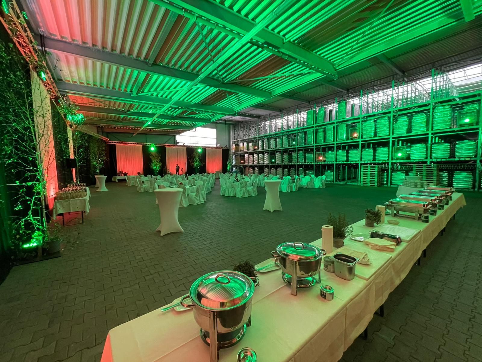 Veranstaltungsraum mit Buffet, Tischen und leuchtend grüner und roter Beleuchtung.