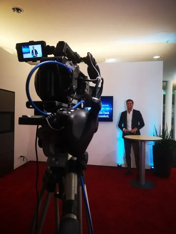 Ein Mann steht vor einer Kamera in einem Raum und moderiert live für das Fernsehen