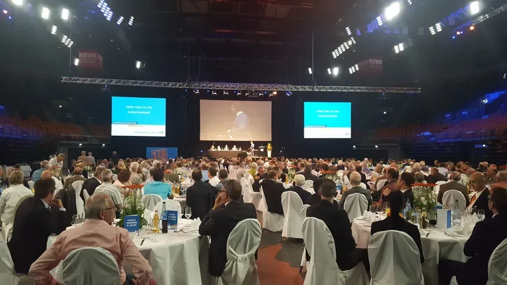 Eine große Gruppe von Menschen sitzt an Tischen und Stühlen in einem großen Saal