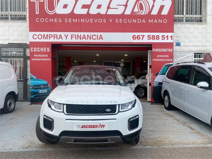 Un Range Rover Evoque blanco está estacionado frente a un concesionario de automóviles.