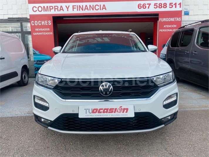 Un Volkswagen T-Roc blanco está estacionado frente a un concesionario de automóviles.