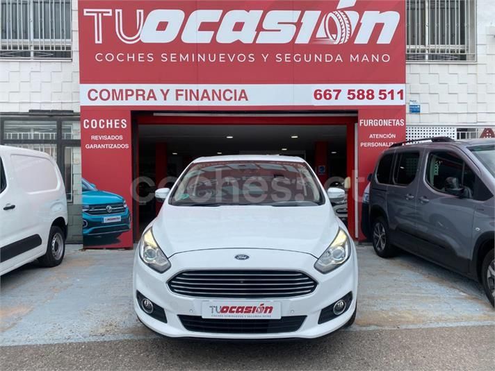 Un coche blanco está aparcado delante de un concesionario de coches de ocasión.