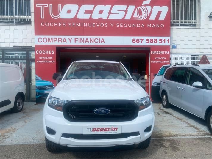 Una camioneta Ford blanca está estacionada frente a un concesionario de automóviles.