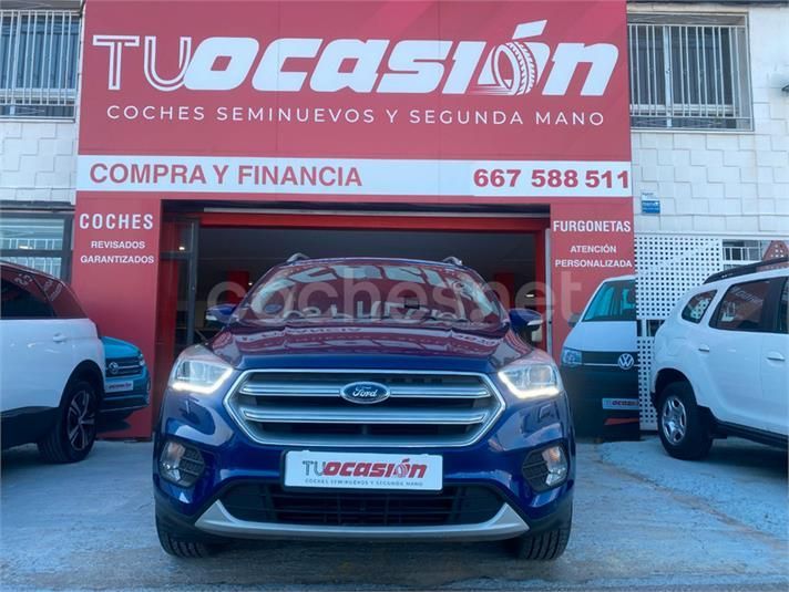 Un coche Ford azul está aparcado delante de un cartel de Tucasion.