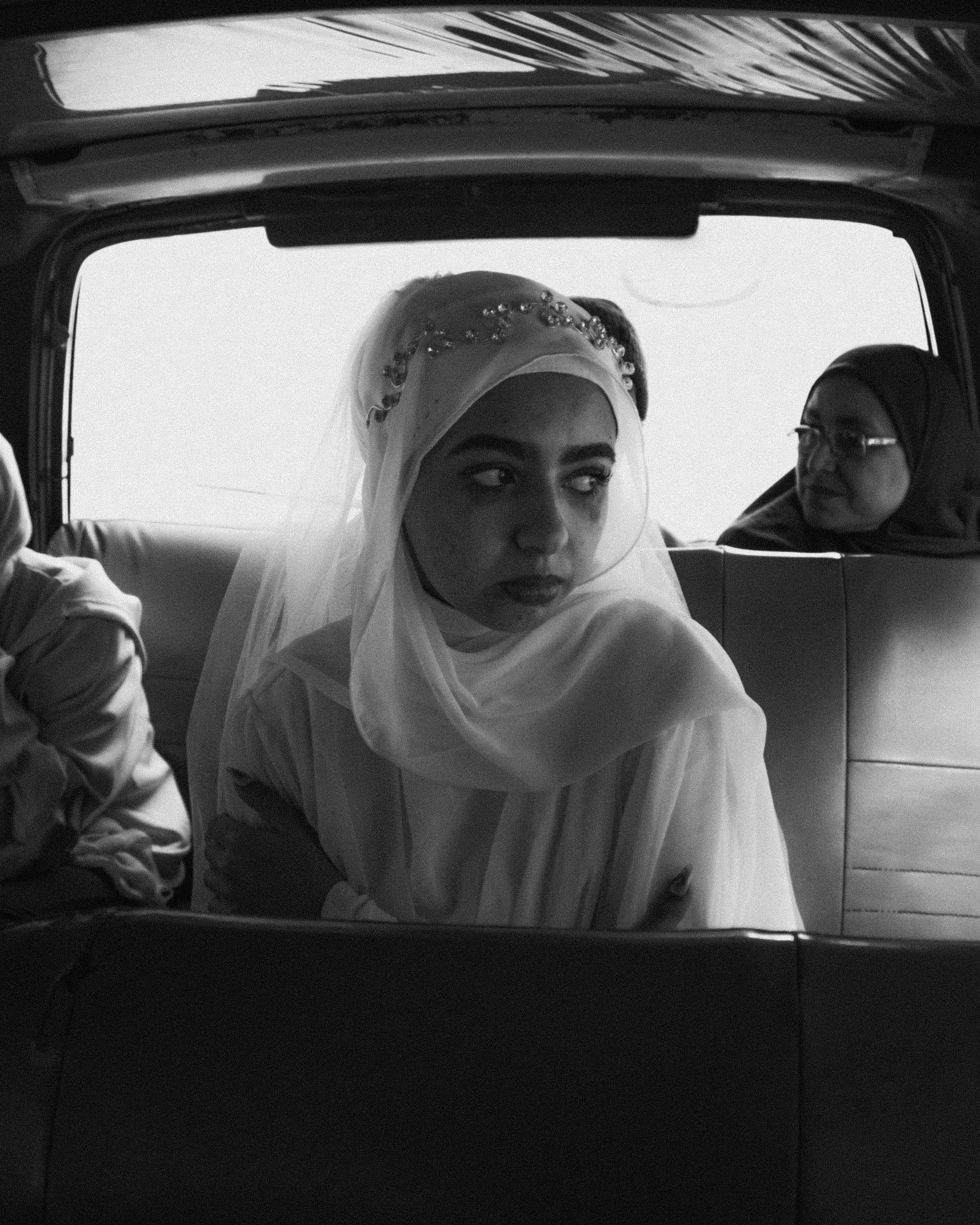 Una mujer con hijab se sienta en el asiento trasero de un coche.