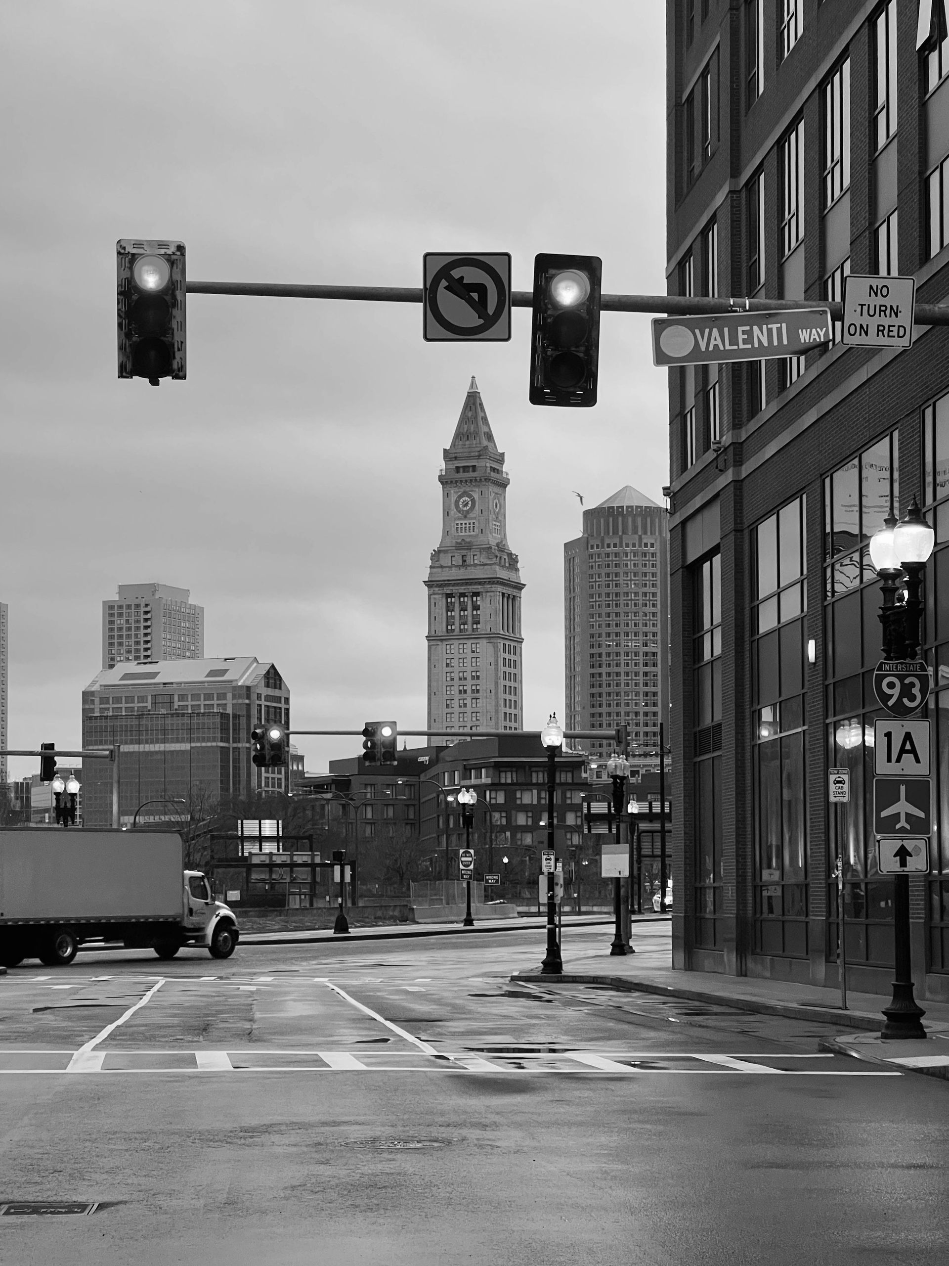 Una fotografía en blanco y negro de una calle de la ciudad con una torre de reloj al fondo.