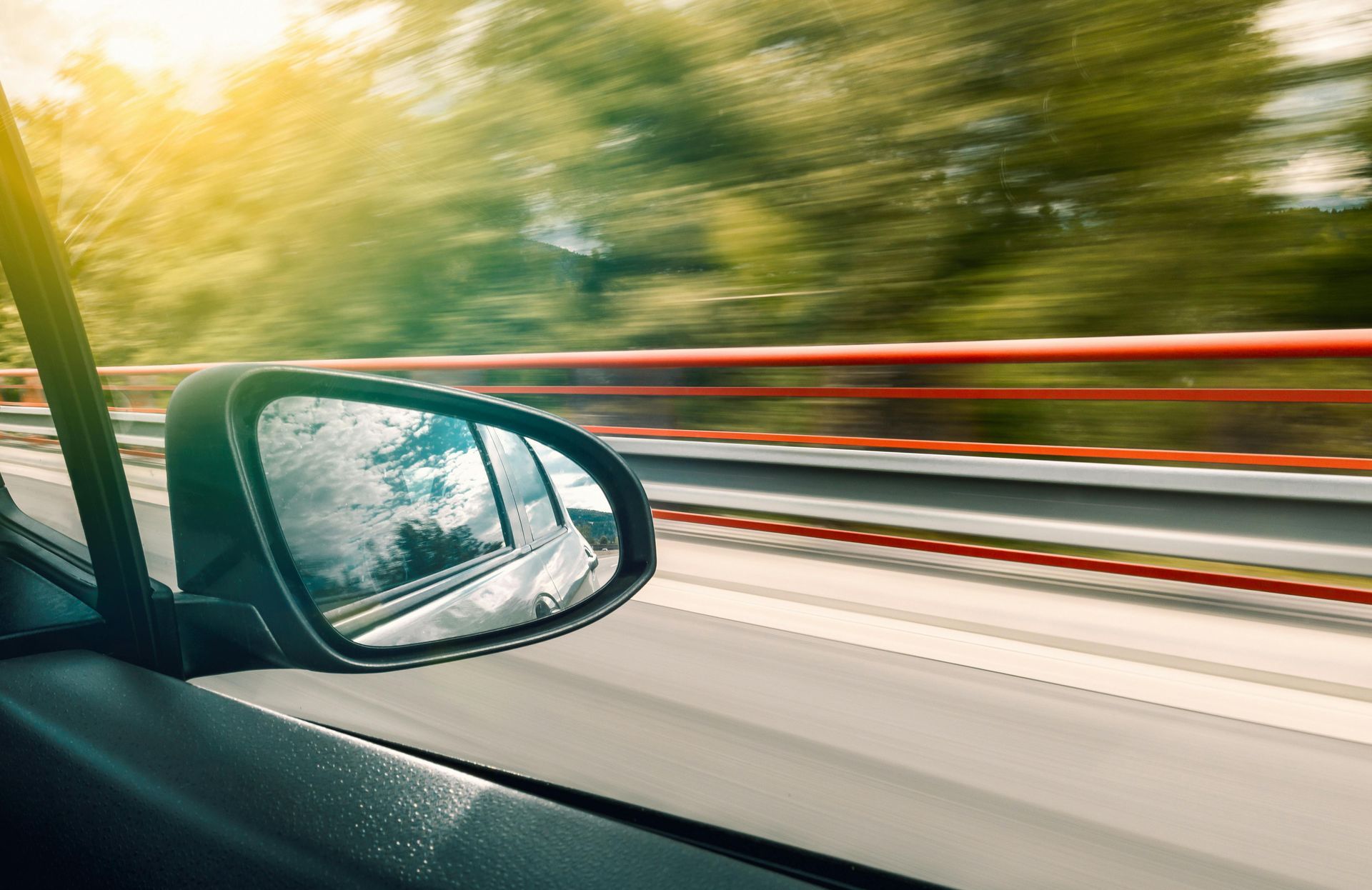 Un automóvil circula por una autopista y se ve el espejo retrovisor.