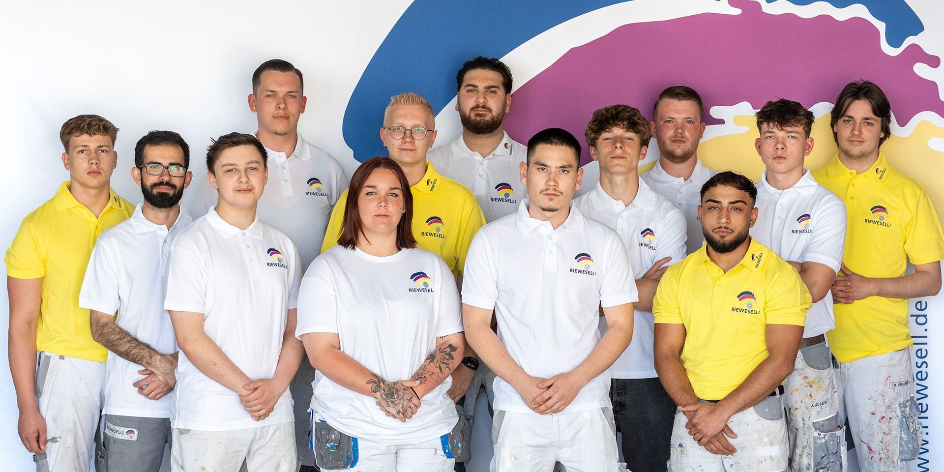 Eine Gruppe von Menschen in weißen und gelben Hemden posiert vor einem farbenfrohen Logo.