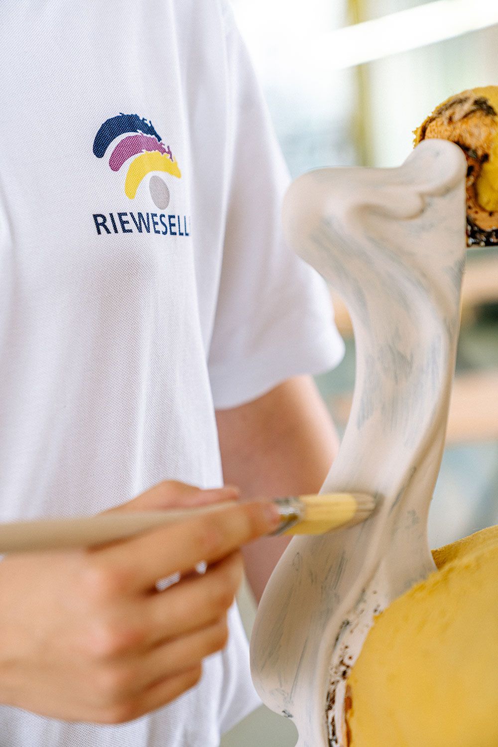 Person in weißem Hemd trägt mit einem Pinsel Schaum auf einen gelben Gegenstand auf.