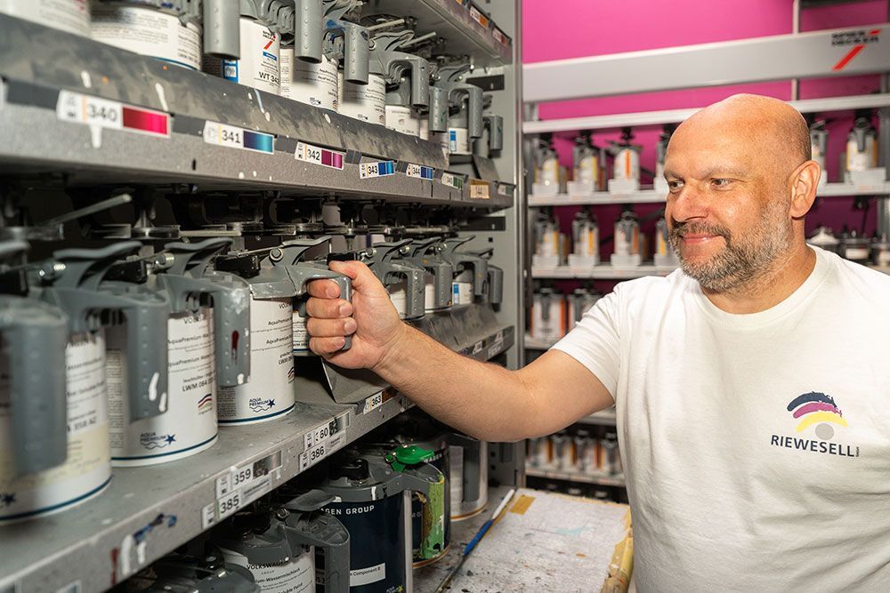 Mann in weißem T-Shirt bedient eine Farbmischmaschine in einem Farbengeschäft.