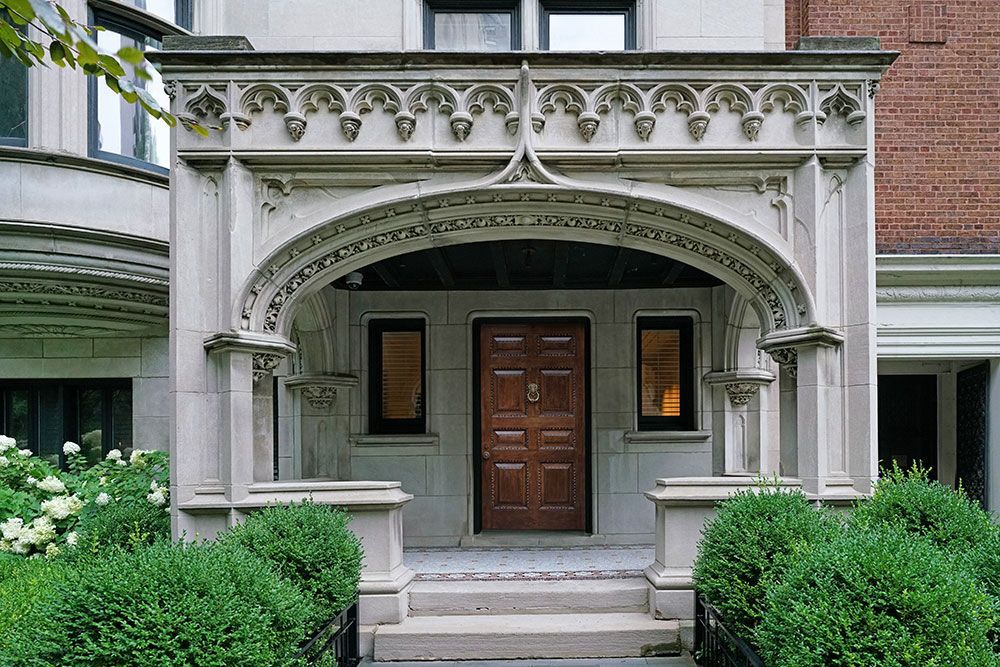 Steingewölbter Eingang mit Holztür, zwei kleinen Fenstern und Heckenbüschen.
