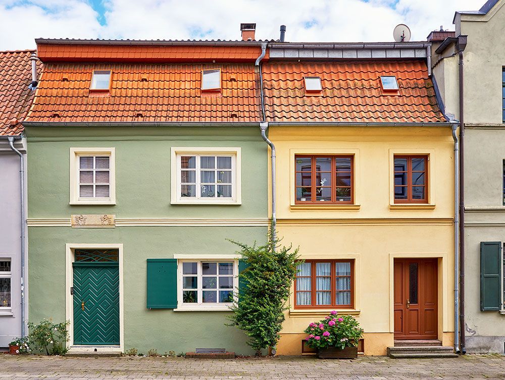 Grüne und gelbe Reihenhäuser mit roten Ziegeldächern.