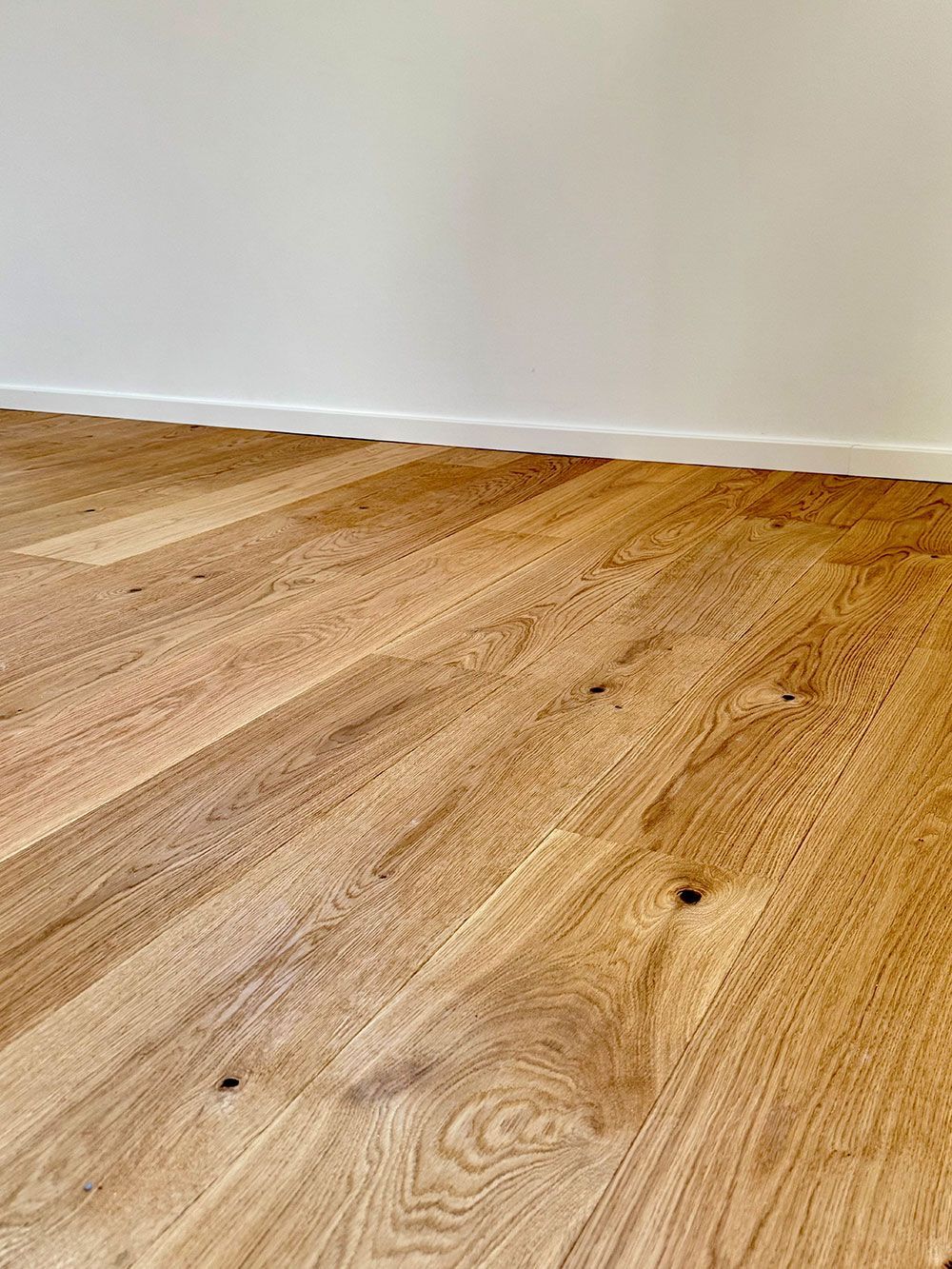 Holzboden im Fischgrätmuster neben einer weißen Wand und Fußleiste.