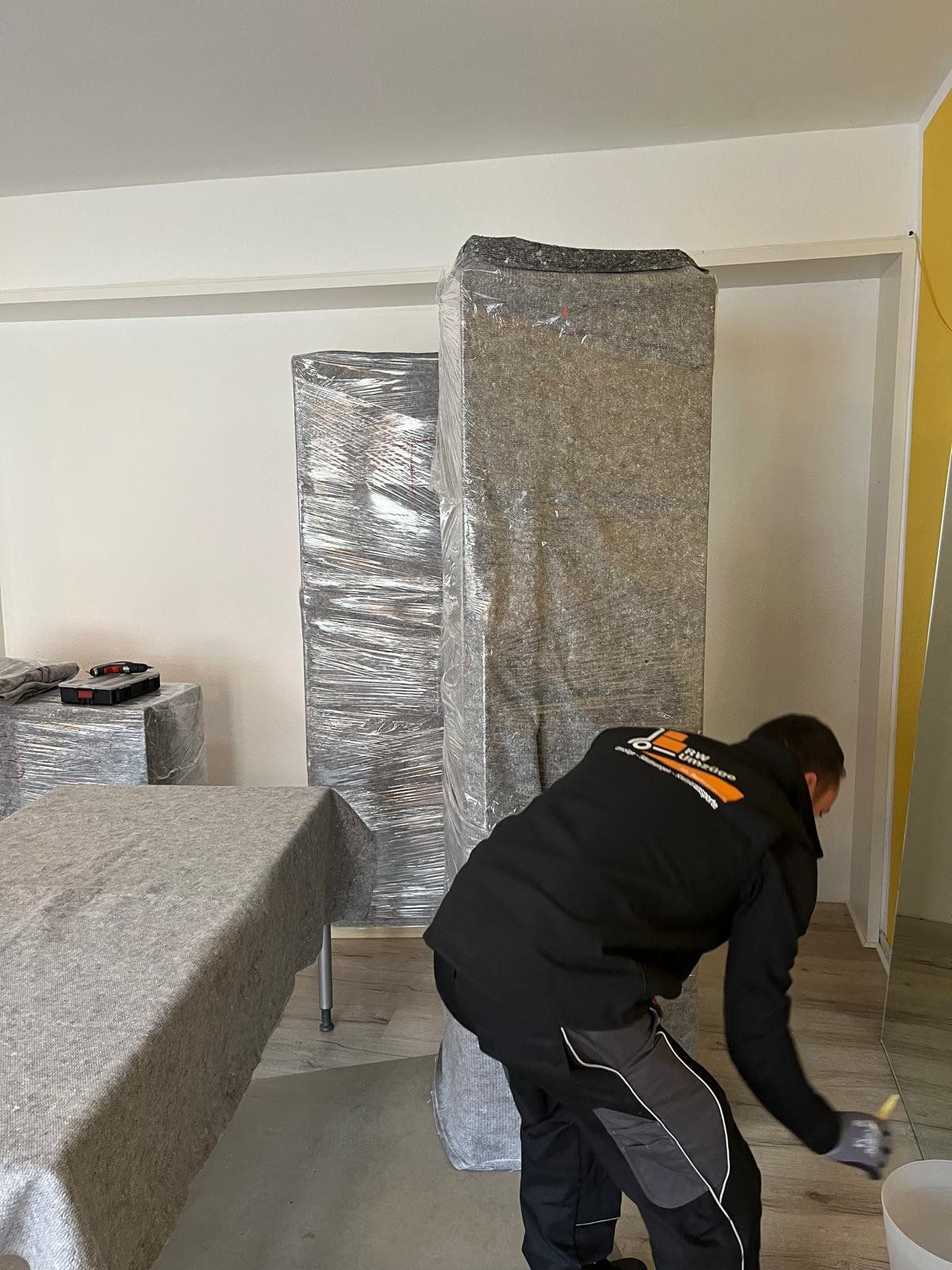 Ein Mann in einer schwarzen Weste streicht eine Wand in einem Raum.