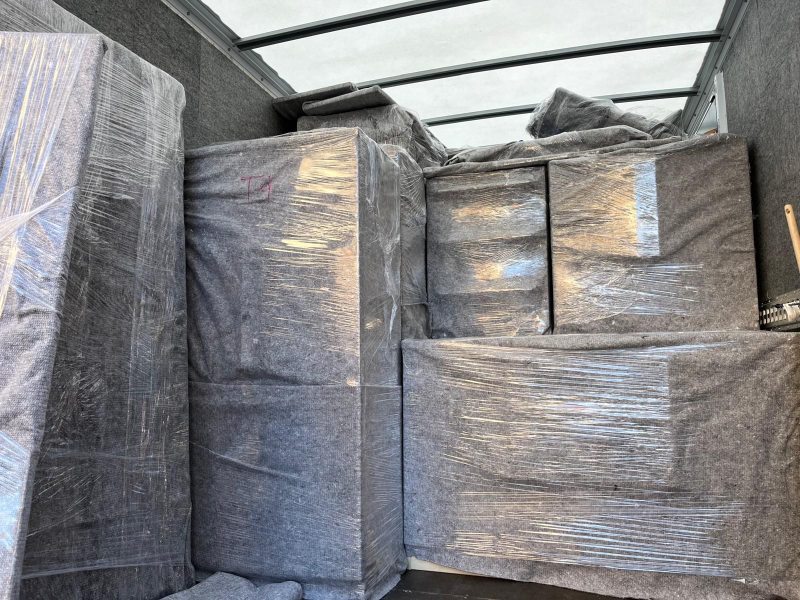 Das Innere eines Umzugswagens voller in Plastik eingewickelter Kisten Möbel.