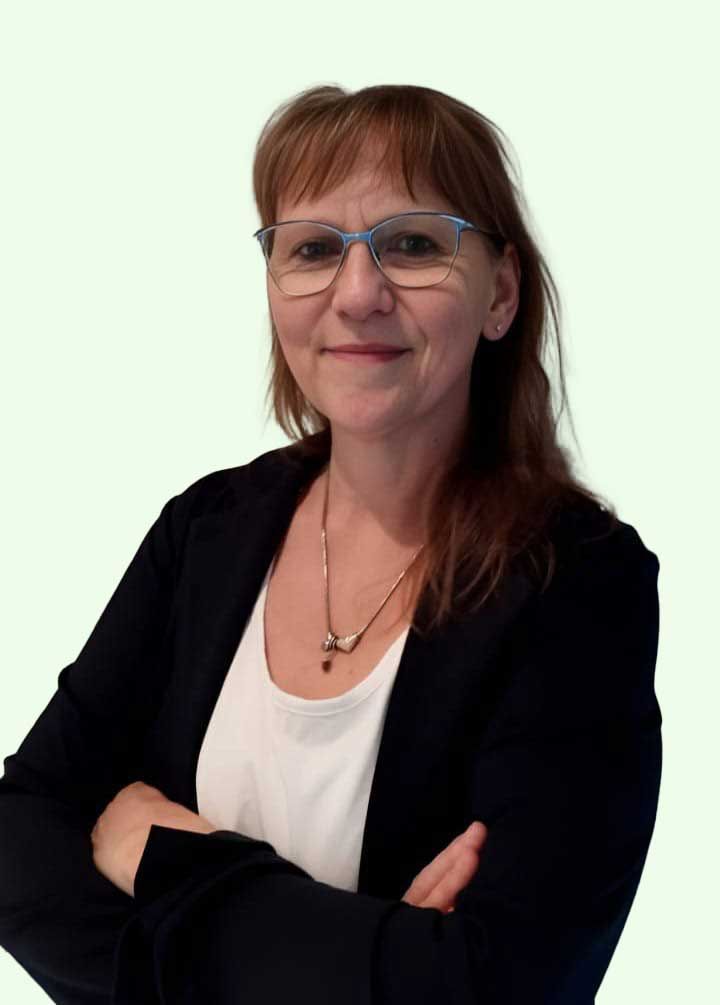 Eine Frau in einem grünen Hemd und einer schwarzen Jacke steht mit verschränkten Armen da.