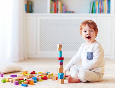 Ein kleiner Junge sitzt auf dem Boden und spielt mit Holzklötzen.