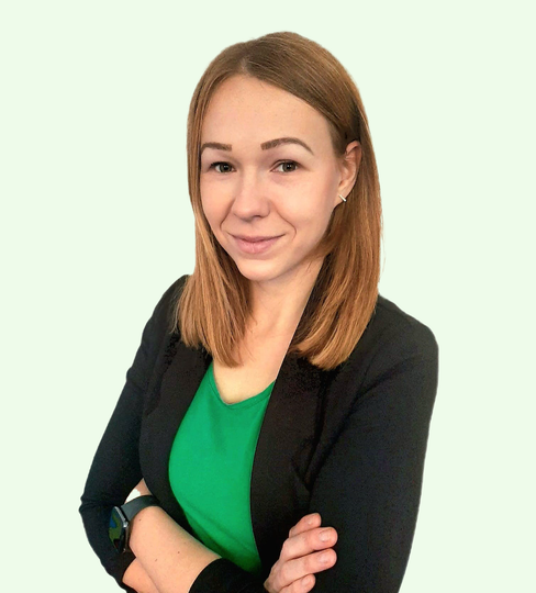 Eine Frau in einem grünen Hemd und einer schwarzen Jacke steht mit verschränkten Armen da.