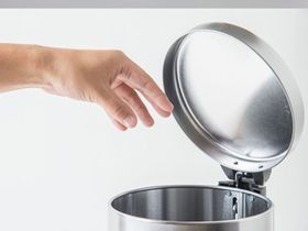 Una persona está tocando la tapa de un bote de basura de acero inoxidable.