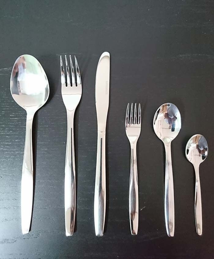 Cubiertos que incluyen cucharas, tenedores y cuchillos sobre una mesa negra