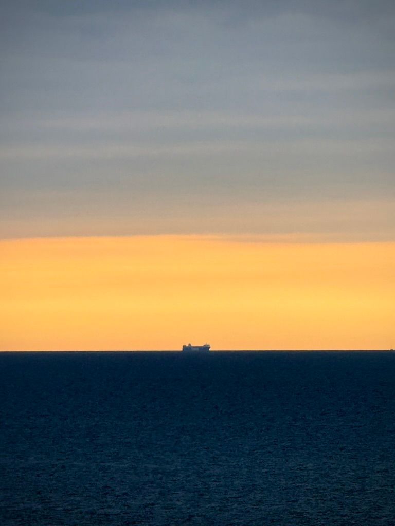 Frachtschiff am Horizont der Ostsee im Morgenrot bei Sierksdorf