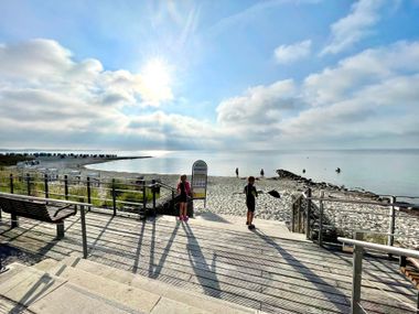 Sonniger Morgen am Sierksdorfer Ostseestrand mit Strandzugang über Holzsteg, Kinder tragen Paddel, Ferienwohnung Traumblick