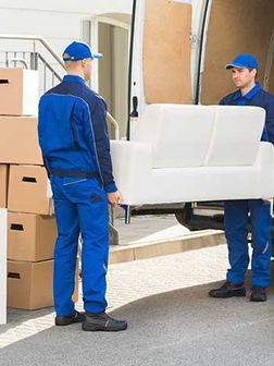 Dos hombres sacan un sofá blanco de una camioneta.