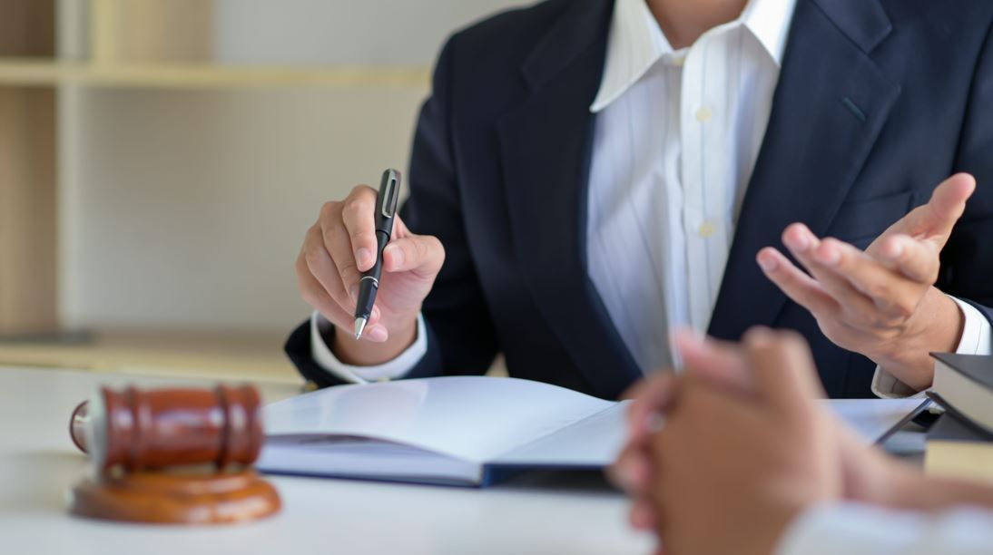 Un profesional del derecho habla con un cliente en un escritorio, con un mazo de madera en primer plano.