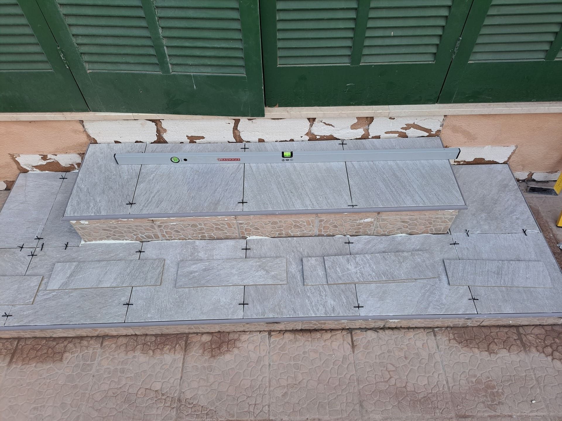 Un conjunto de escalones que se están construyendo frente a una ventana con contraventanas verdes.