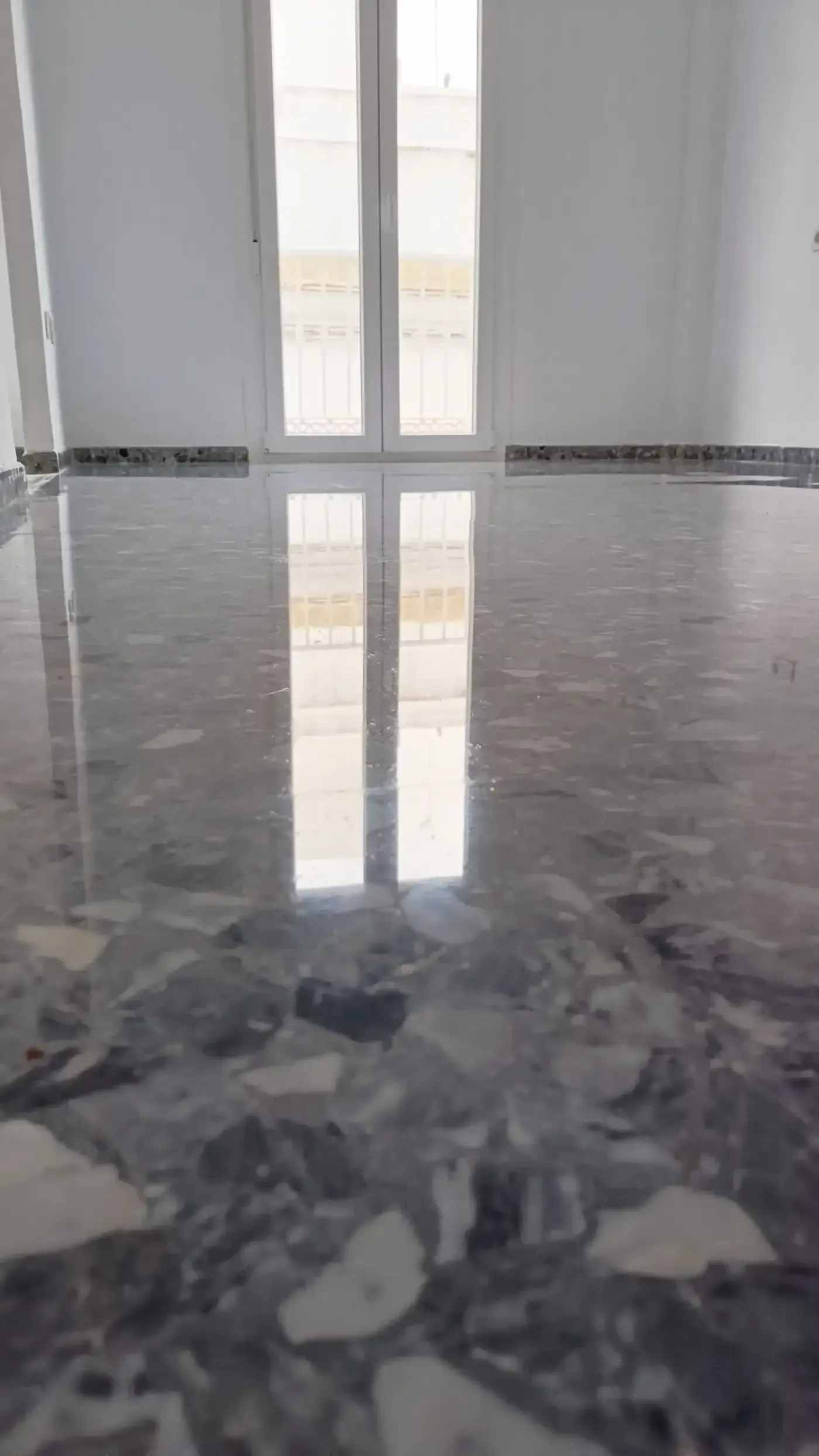 Piso de piedra gris pulida que refleja una ventana alta; paredes blancas, luz natural.