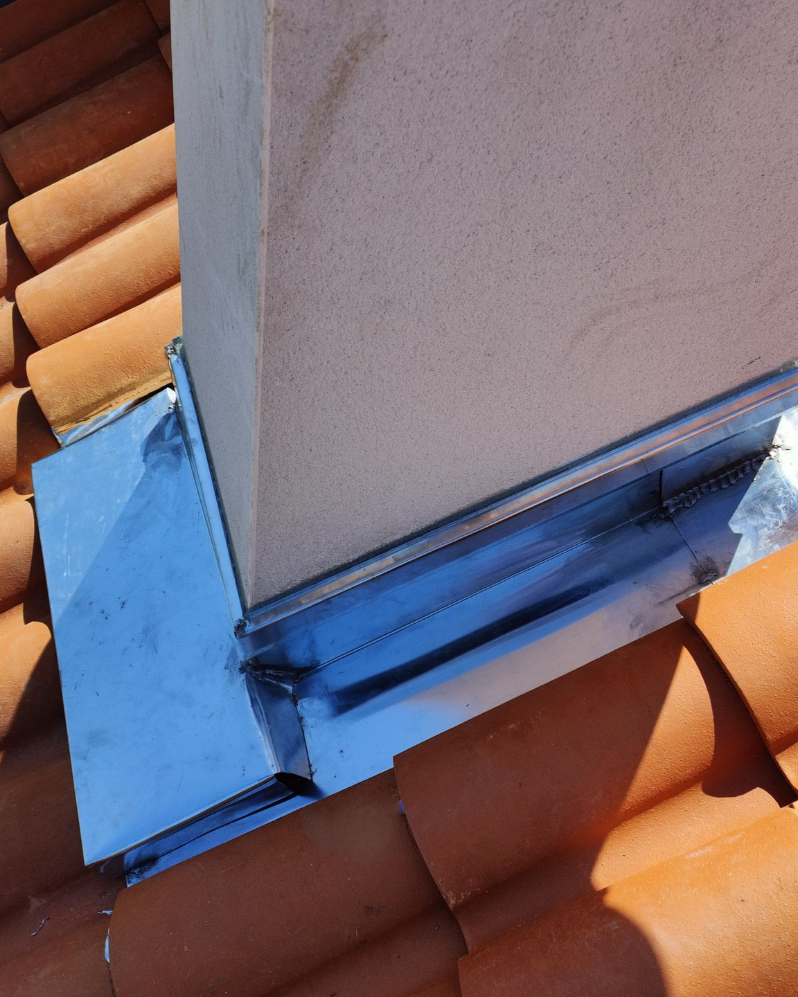 Cheminée avec solin métallique sur un toit de tuiles.