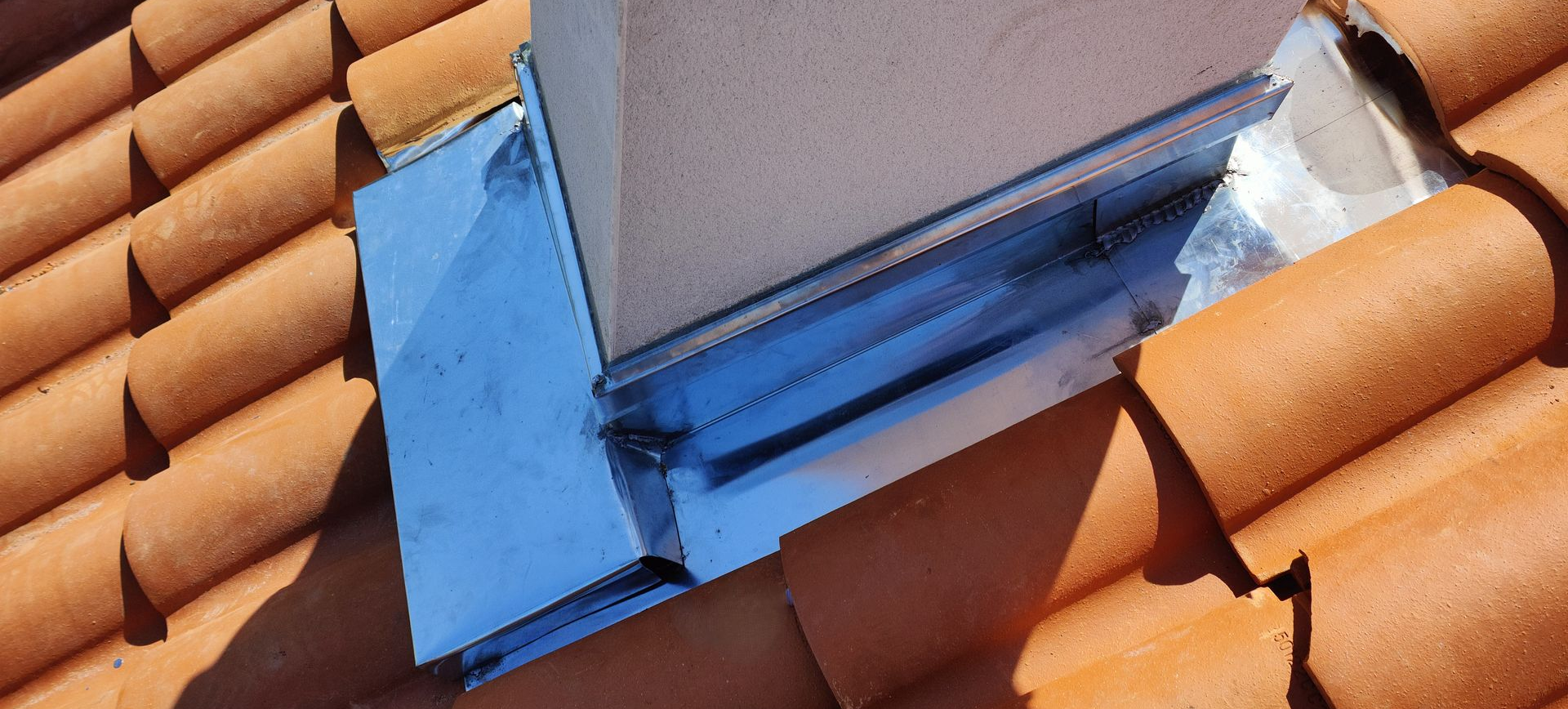 Solin métallique autour d'une cheminée sur un toit de tuiles en terre cuite.