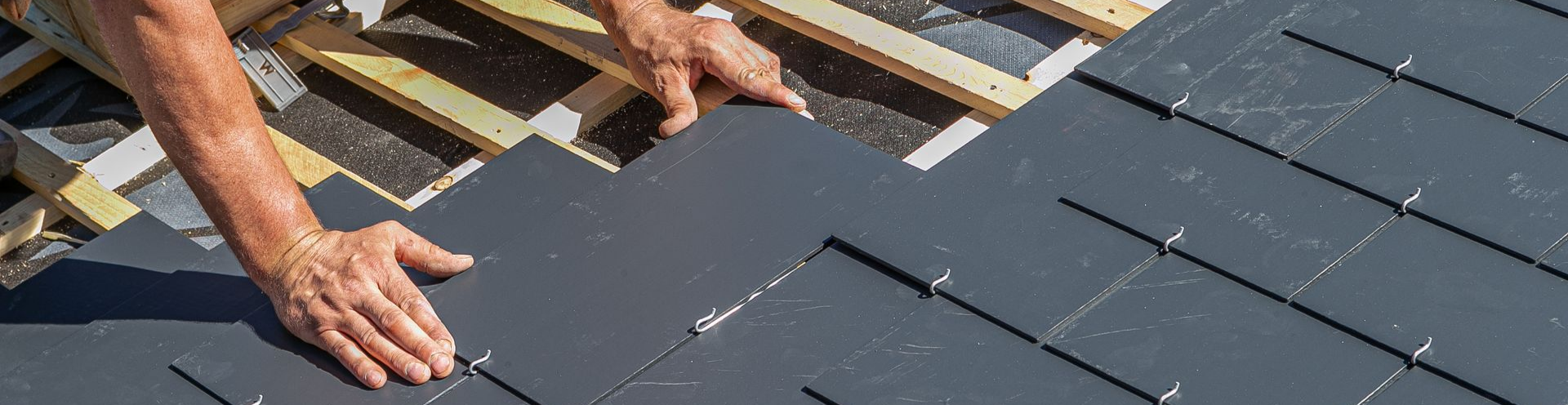 Une personne installant des tuiles grises sur une structure en bois.