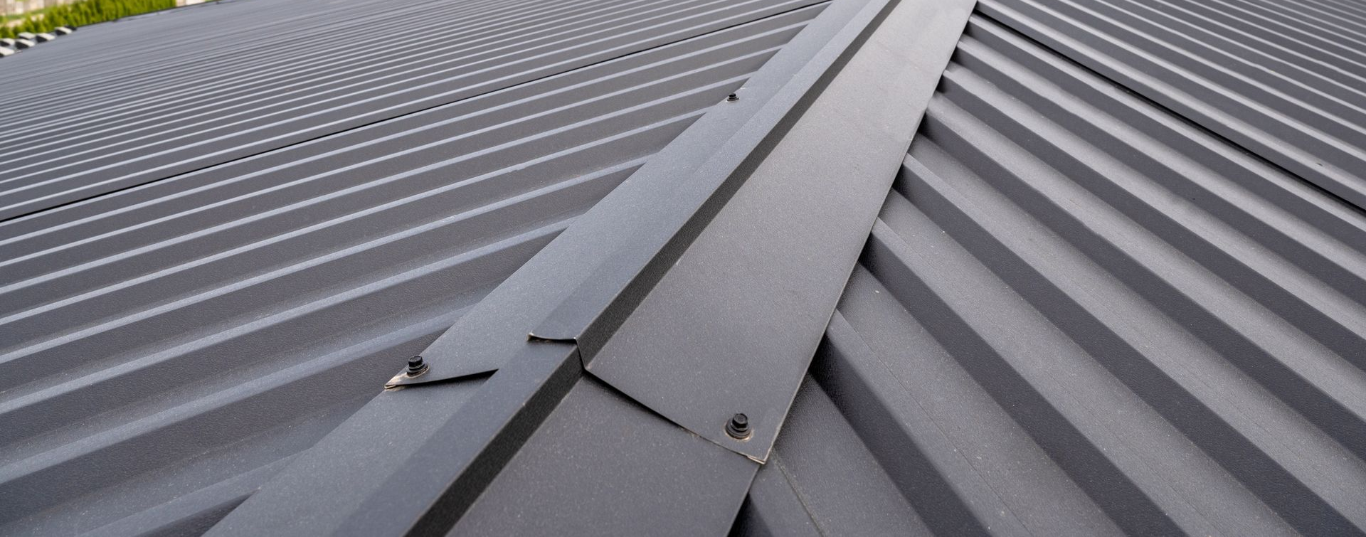Gros plan sur une toiture métallique grise avec des panneaux ondulés et une faîtière.