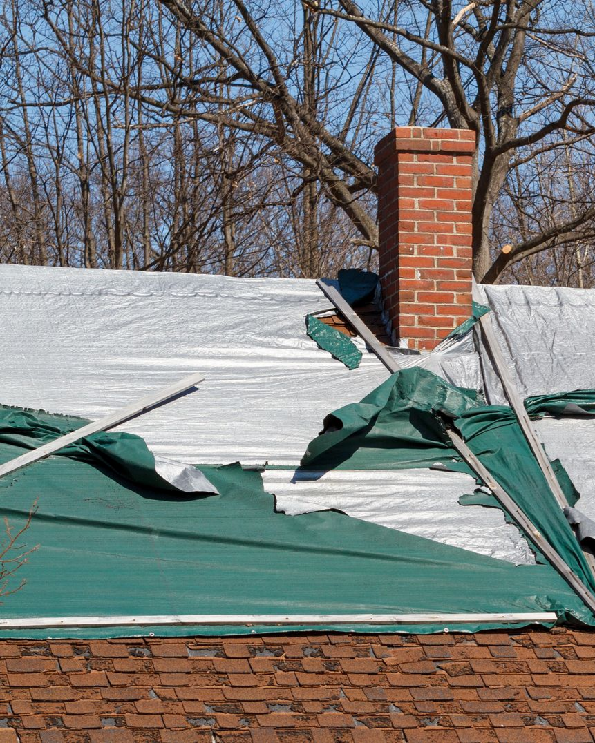 Toiture endommagée avec couverture verte déchirée et cheminée en briques rouges.