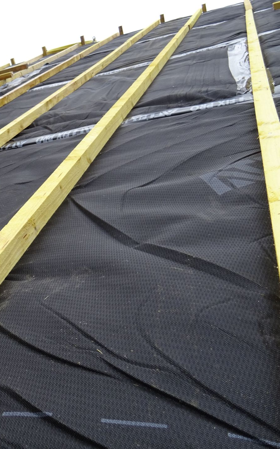 Pose d'une sous-couche de toiture noire sur les chevrons.