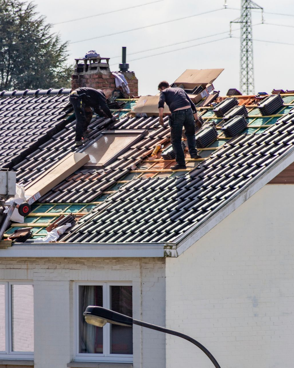 Des couvreurs travaillent sur le toit d'une maison, remplaçant des tuiles. Lumière du soleil, ciel bleu et poteau électrique en arrière-plan.
