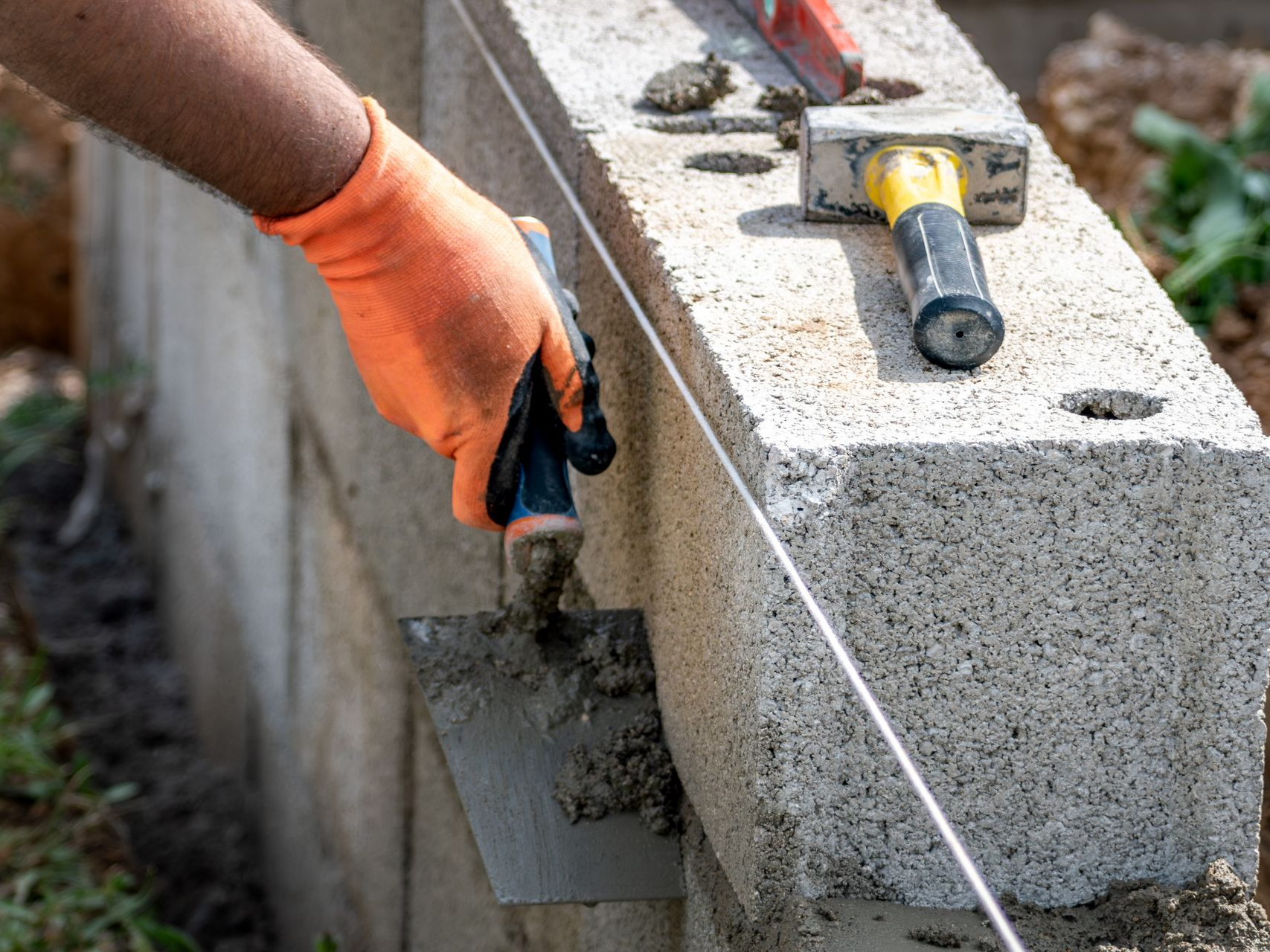 Une main gantée d'orange utilise une truelle pour appliquer du mortier sur un bloc en béton.