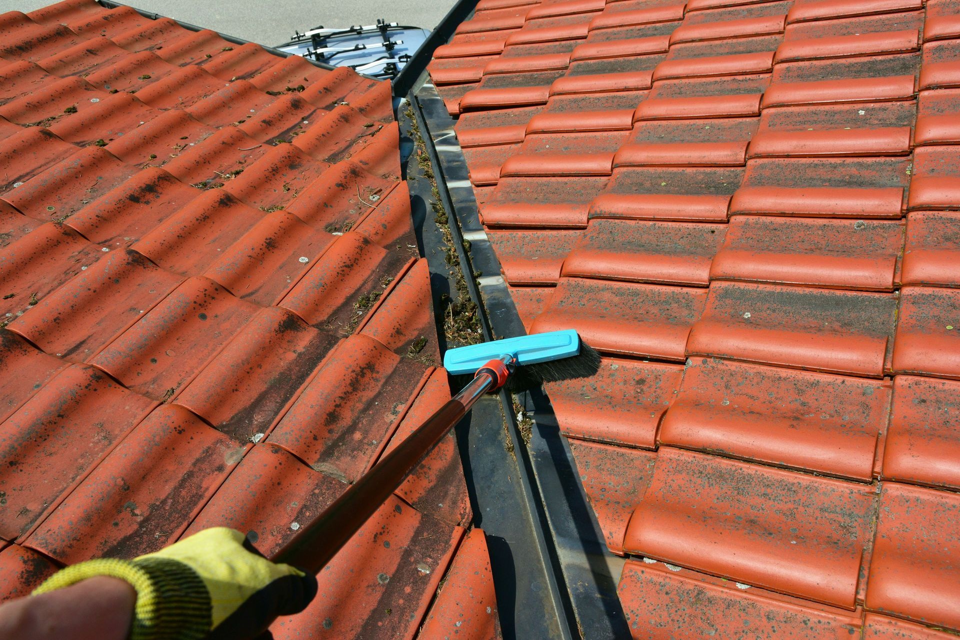 Une personne portant un gant jaune utilise un outil à long manche pour dégager les débris d'une gouttière.