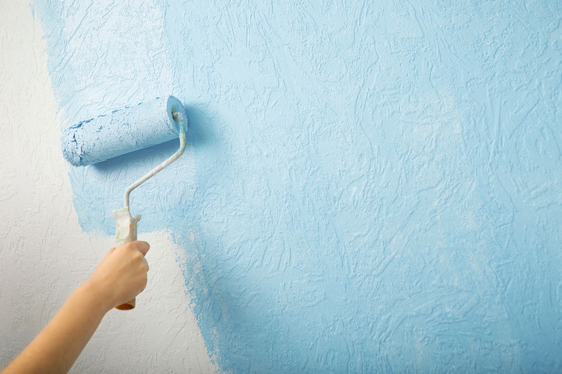 Une personne peint un mur avec un rouleau à peinture bleu.