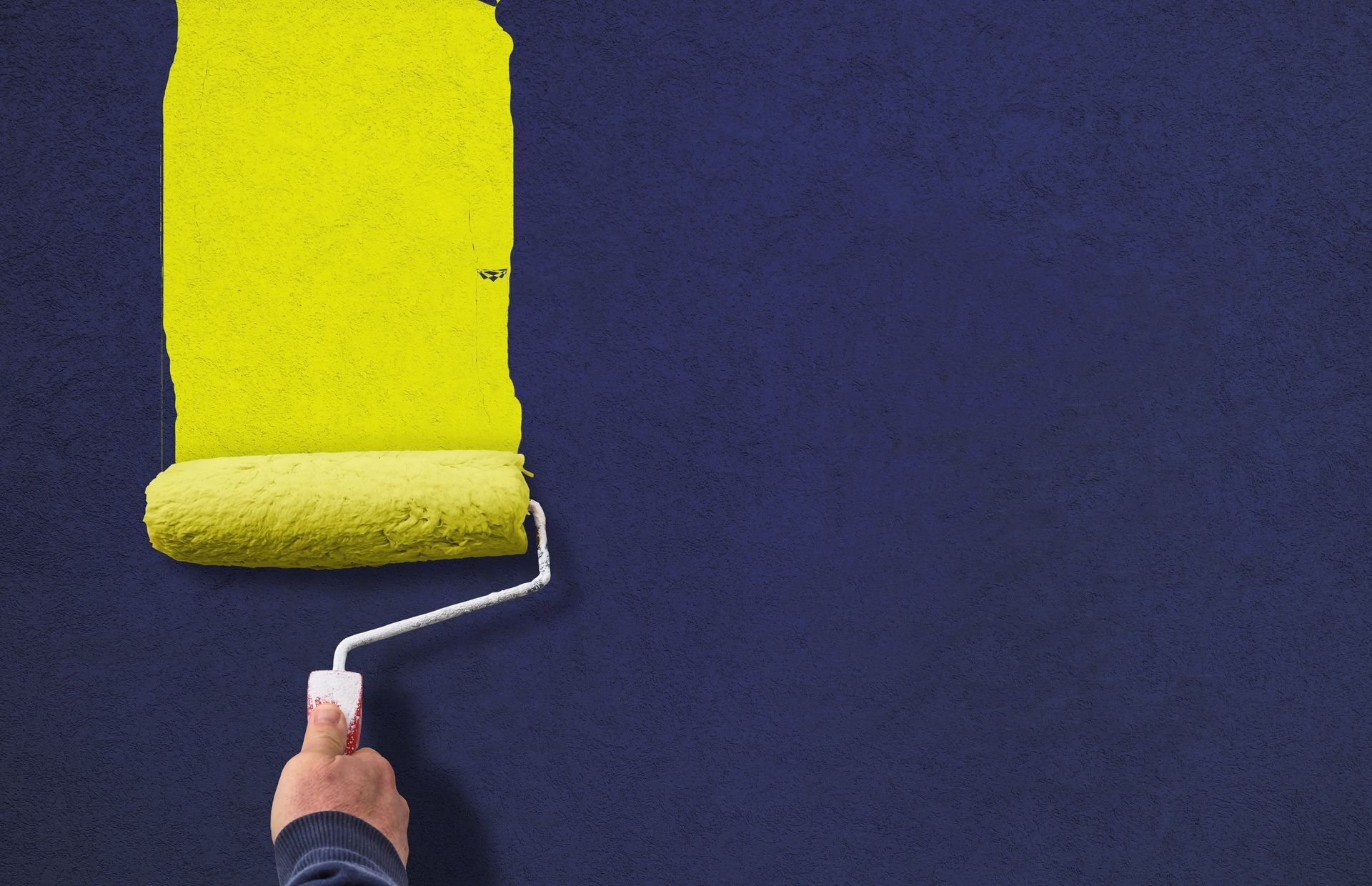 Une personne peint un mur avec un rouleau à peinture jaune.