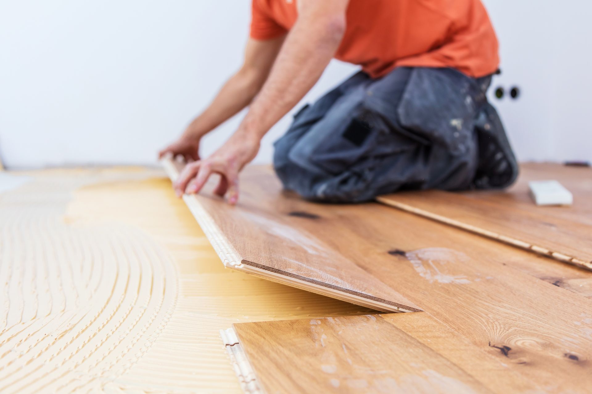 Un homme s'agenouille pour installer un plancher en bois.