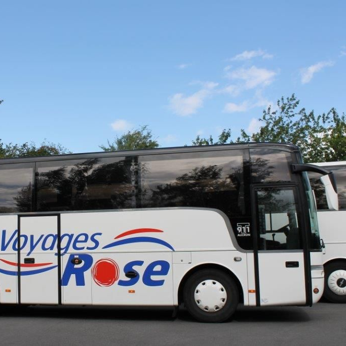 Un bus blanc Voyages Rose est stationné sous un ciel bleu, avec quelques arbres en arrière-plan.