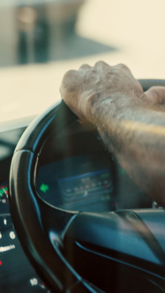 Une main posée sur un volant noir, à l'intérieur d'un véhicule.