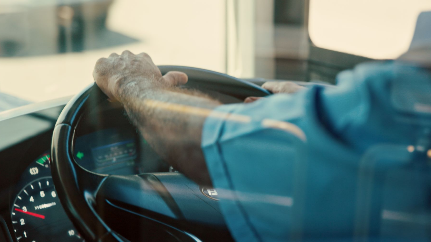 Un conducteur de bus en chemisette bleue a les mains sur le volant.
