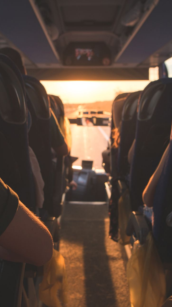 À l'intérieur d'un bus, vue sur une route au coucher du soleil ; des personnes sont assises.