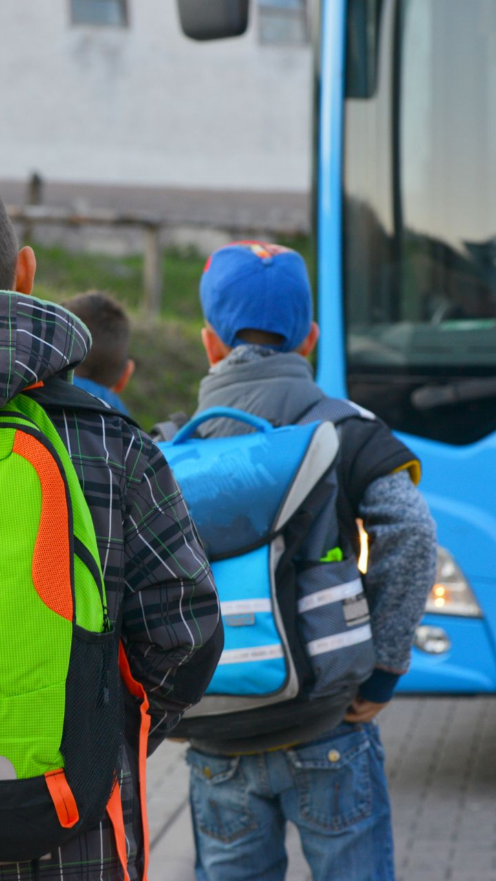 Des enfants attendent près d'un bus bleu, portant des sacs à dos.